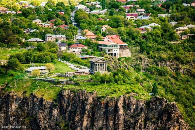 Temple of Garni perched on basalt cliffs above Garni village in Kotayk Province, Armenia, with green hills and village houses in spring.