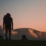 Solo traveler with backpack hiking at sunrise in the mountains, symbolizing independence and adventure