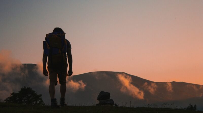 Solo traveler with backpack hiking at sunrise in the mountains, symbolizing independence and adventure