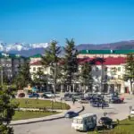 Tskhinvali city center with cars, Soviet-style buildings, and Caucasus mountains in the background