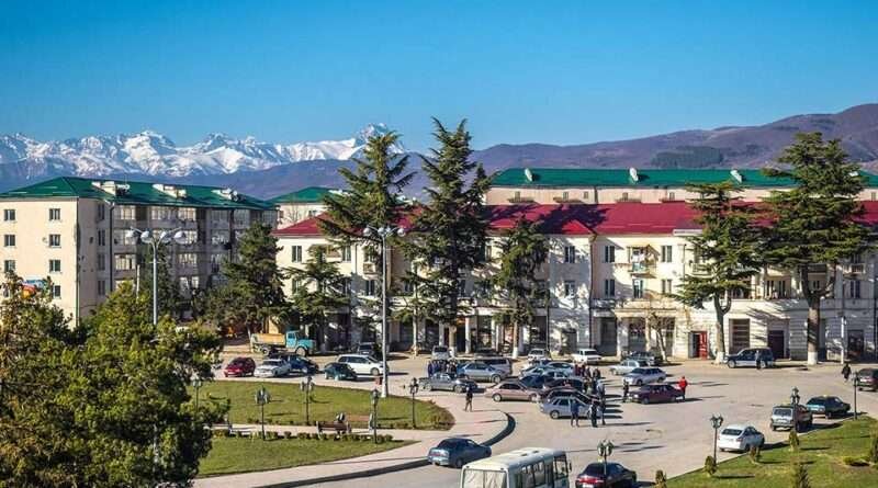 Tskhinvali city center with cars, Soviet-style buildings, and Caucasus mountains in the background
