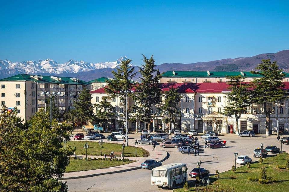 Tskhinvali city center with cars, Soviet-style buildings, and Caucasus mountains in the background
