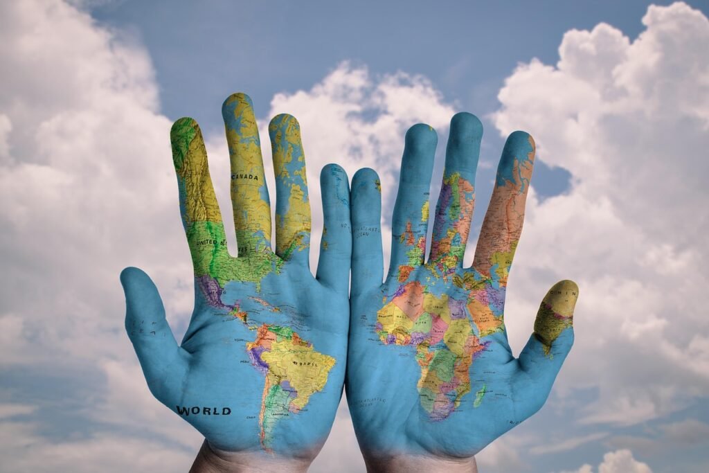 World map painted on two open hands against a cloudy sky, symbolizing people–environment relationships at the heart of geography.