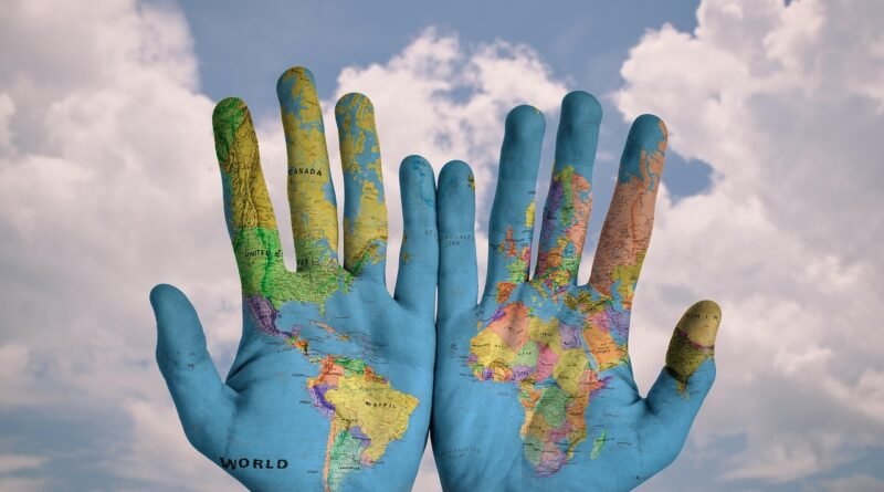 World map painted on two open hands against a cloudy sky, symbolizing people–environment relationships at the heart of geography.