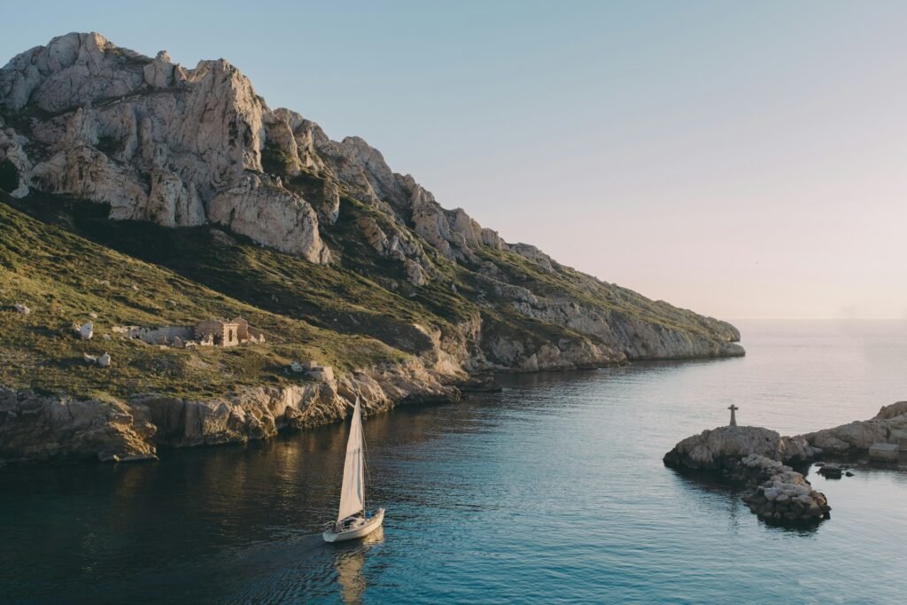 Sailboat entering a limestone calanque near Marseille at golden hour, Provence, France.