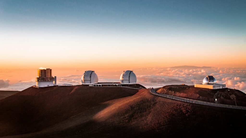 Mauna Kea observatories at sunset above the clouds on Hawaiʻi Island, telescope domes lining the ~13,800-ft (4,207-m) summit ridge