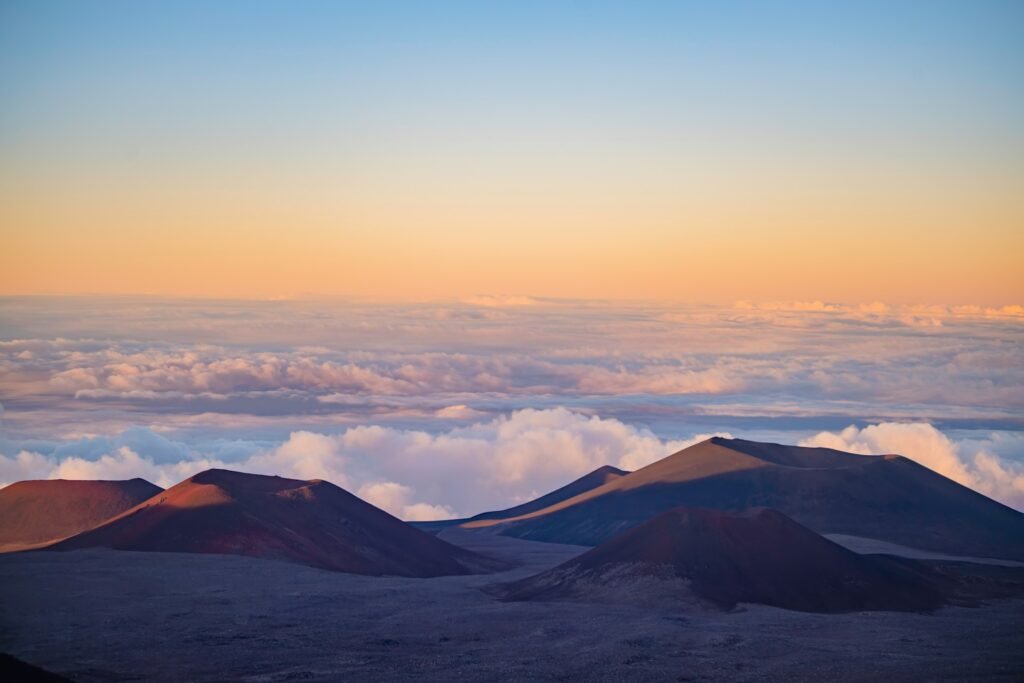 Mauna Kea summit cinder cones above a sea of clouds at sunrise, illustrating the mountain’s base-to-summit height from the Pacific seafloor