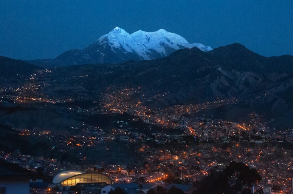 Night view of La Paz, Bolivia—city lights filling a steep Andean valley beneath snowcapped Mount Illimani; world’s highest capital at 3,650 m (11,975 ft).