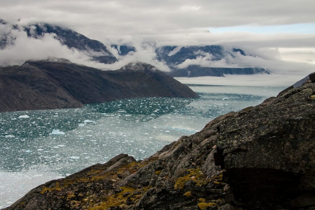 Greenland fjord filled with drift ice below cloud-wrapped mountains