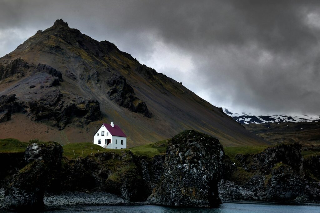 Remote farmhouse beneath steep volcanic slopes on a stormy coastline, Westfjords, Iceland.