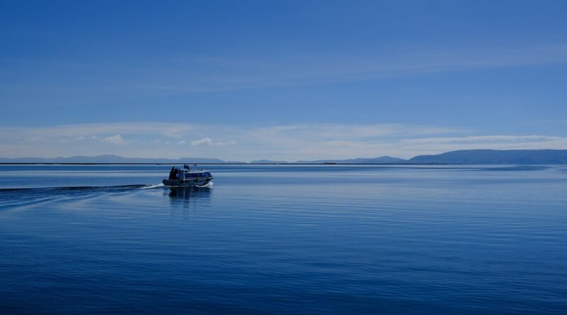 Boat crossing the deep-blue waters of Lake Titicaca with Andean hills on the horizon under a clear sky.