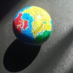 Small globe lit by sunlight on a dark textured surface, showing Europe, North Africa, Greenland/Canada—concept image of global scope.