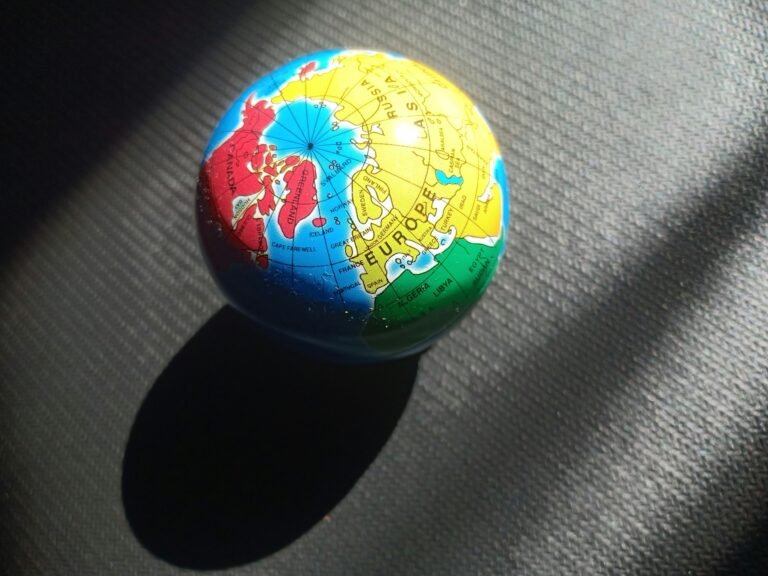 Small globe lit by sunlight on a dark textured surface, showing Europe, North Africa, Greenland/Canada—concept image of global scope.