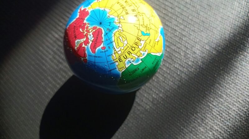 Small globe lit by sunlight on a dark textured surface, showing Europe, North Africa, Greenland/Canada—concept image of global scope.