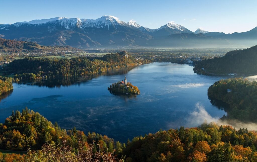 Lake Bled, Slovenia—calm blue water with a small island church, autumn forests, morning mist, and the snow-capped Julian Alps in the background; a clear example of a natural inland lake.