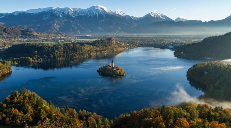 Lake Bled, Slovenia—calm blue water with a small island church, autumn forests, morning mist, and the snow-capped Julian Alps in the background; a clear example of a natural inland lake.