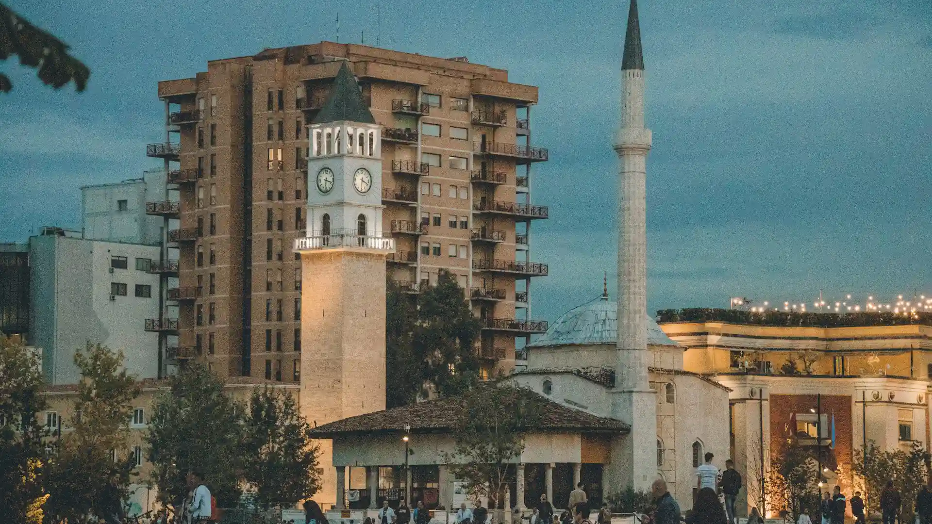 Evening view of Tirana with clock tower, mosque and apartment buildings.