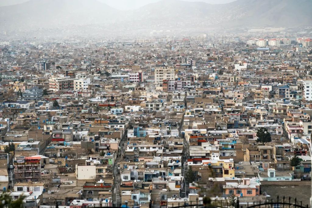 Wide aerial view of Kabul, Afghanistan, with dense low-rise neighborhoods spreading across a mountain-ringed valley.