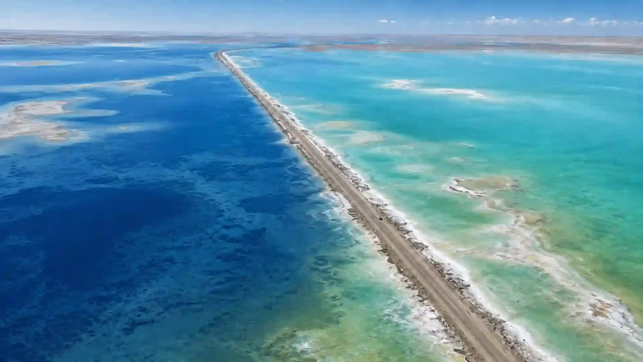 Aerial view of G315 dividing deep-blue and turquoise-green water at Xitai Jinaier Lake in Qinghai’s Qaidam Basin.