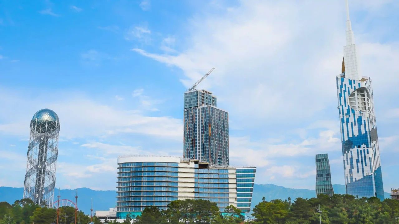 Batumi skyline with Alphabet Tower on the left, modern high-rises, green trees and mountains in the background.