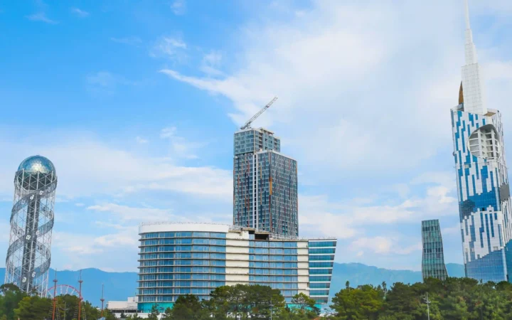 Batumi skyline with Alphabet Tower on the left, modern high-rises, green trees and mountains in the background.